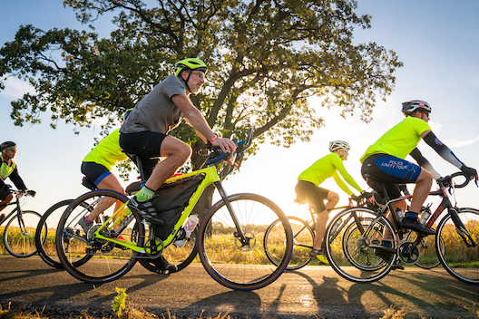 Side view of people riding bikes on a road, wearing helmets. 