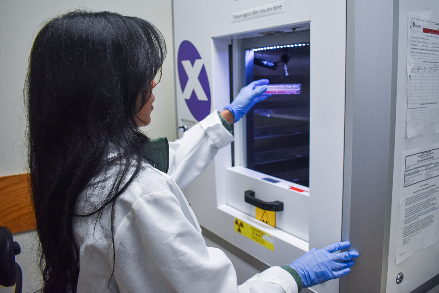 Female lab member puts petri dish in machine
