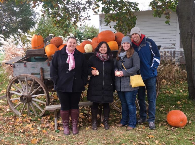 Four people smile next to pumpkin cart