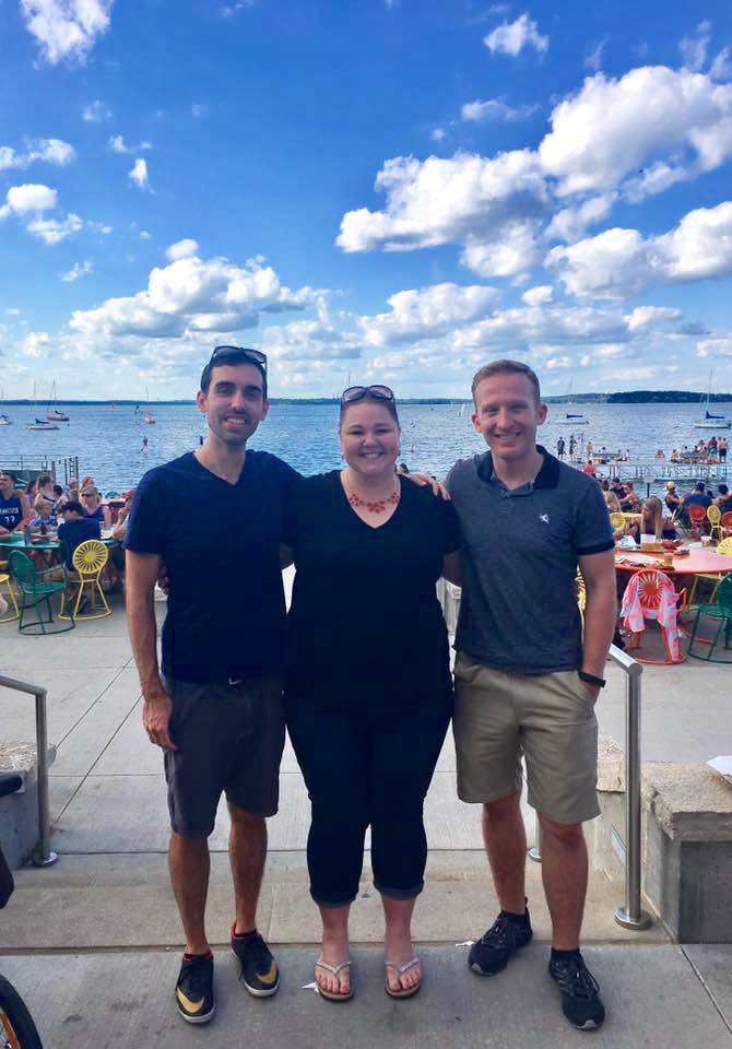 three people smile on terrace by lake