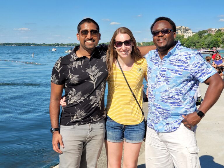 Three people smile in the sunshine near the lake