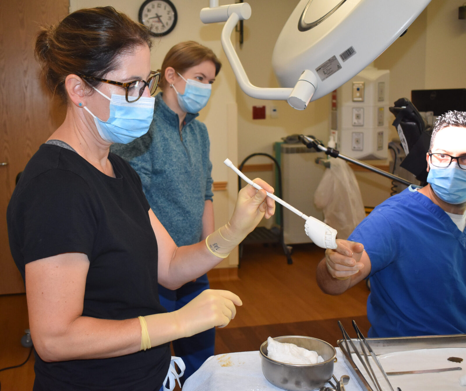 three doctors work in an OR handing tools to each other