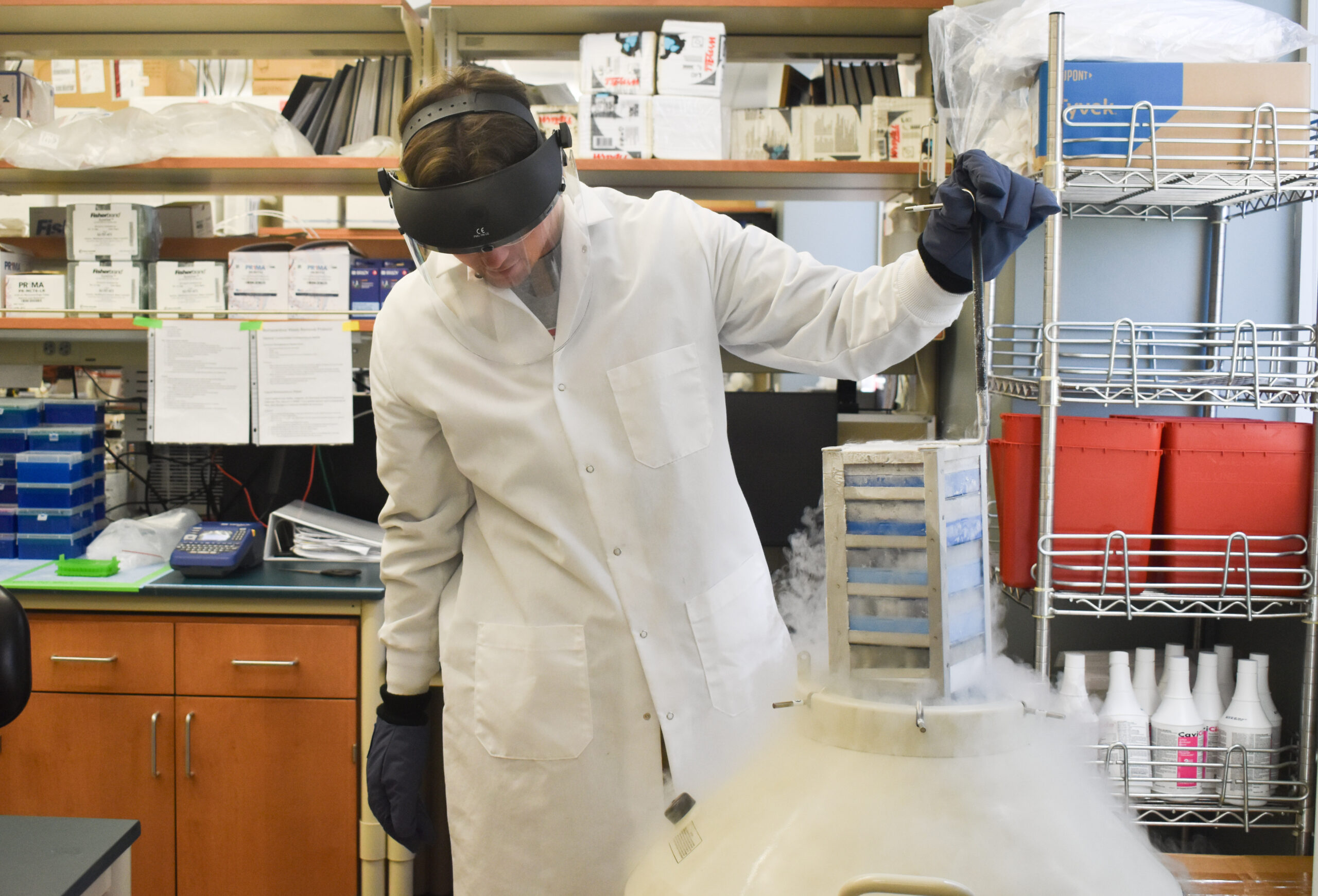 Man with face shield holds frozen sample with gloves